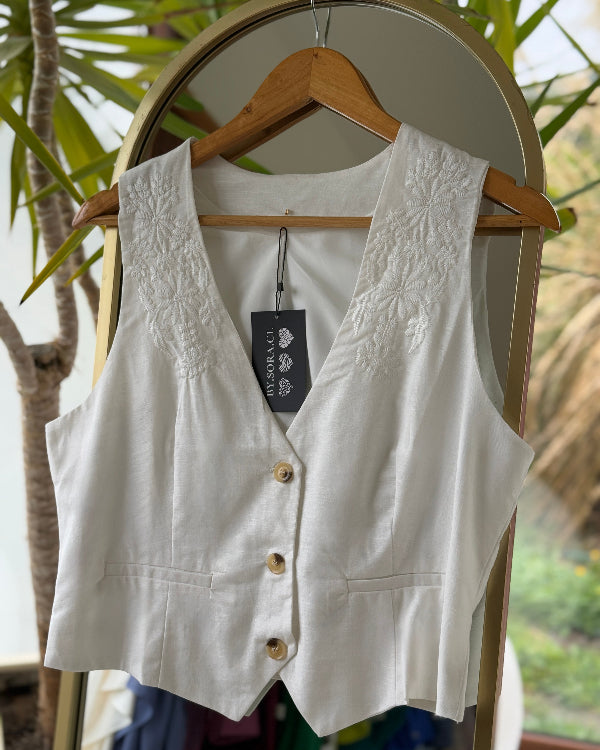 Vest Lino Bordado en perchero rodeado de plantas